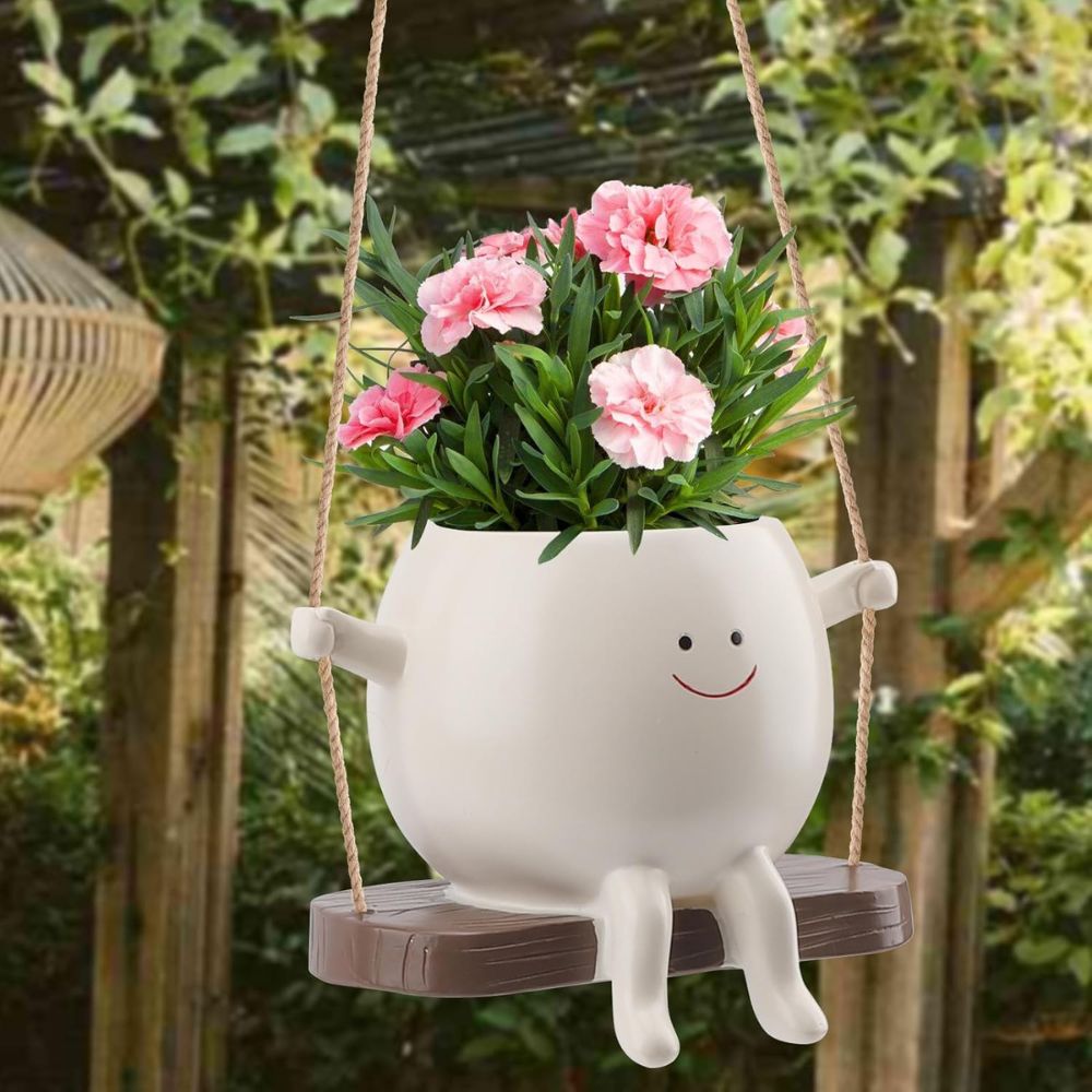 White planter with pink flowers on a swing in a garden setting